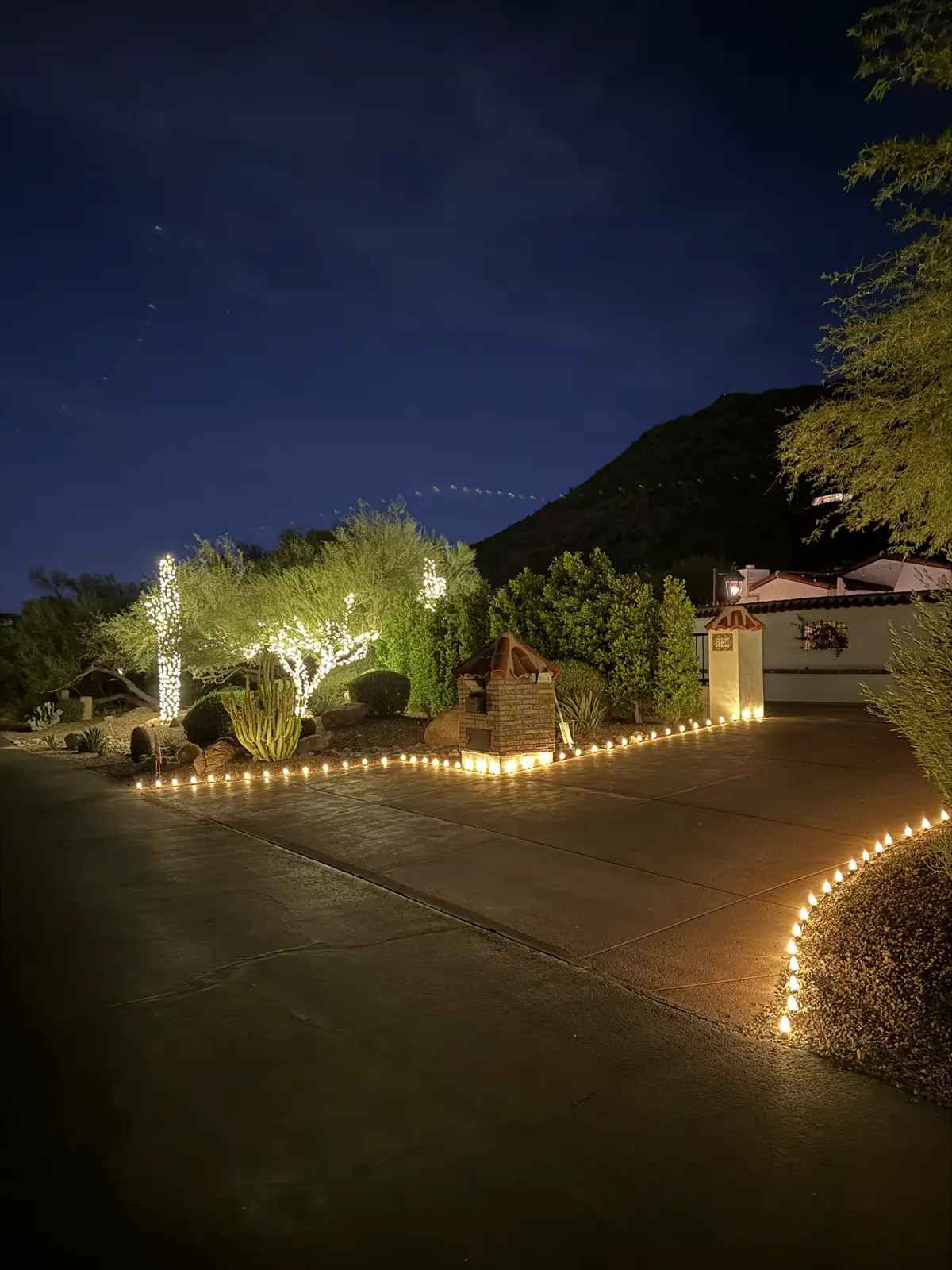 Driveway lined with glowing lights below a desert mountain