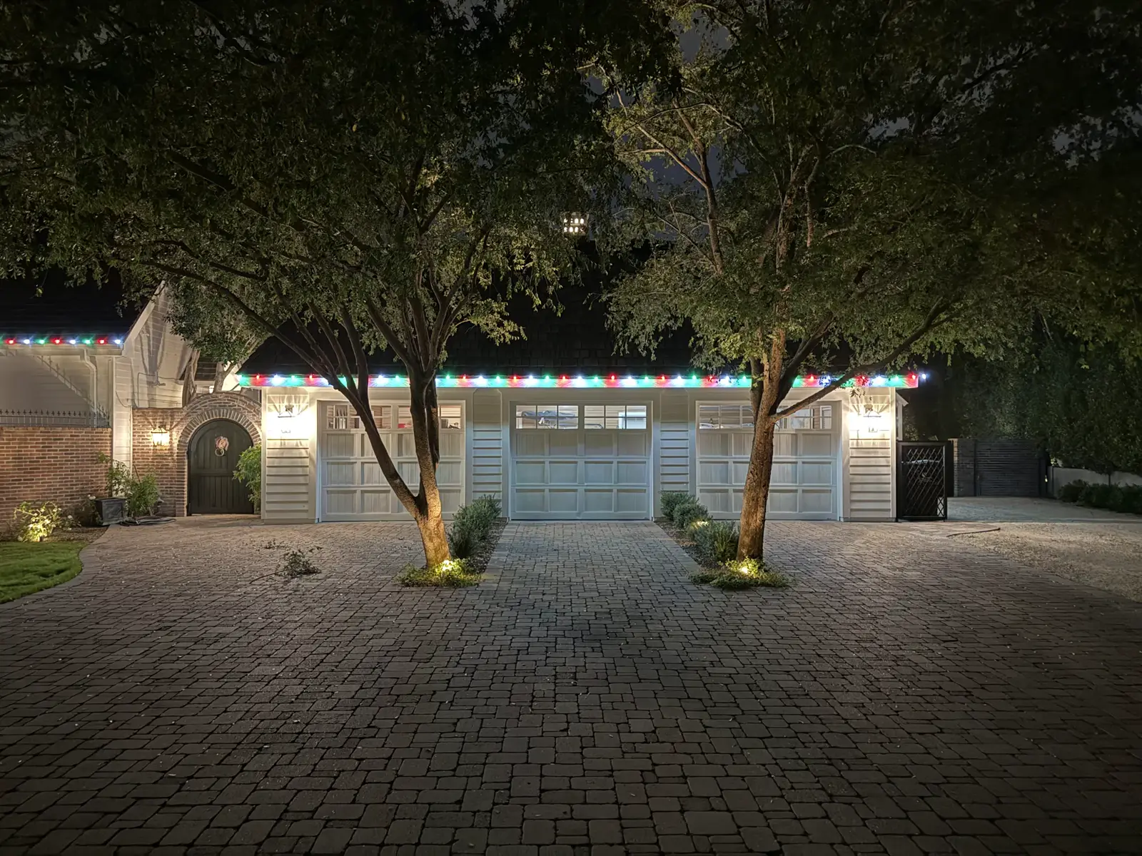 Courtyard home with lit roofline behind two trees and a paver drive