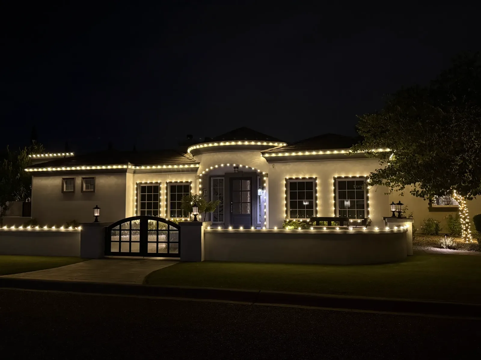 A stucco home with warm white lights outlining every roofline, window, arch and front wall, installed by BM Christmas Lights